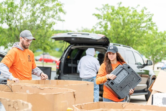 Two people, both in orange shirts, load old electronics into bins at an E-cycle Wisconsin event. 