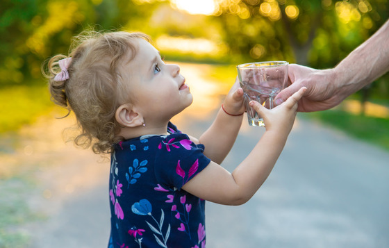 A child drinks grab a glass of clear water that is handed to her. 