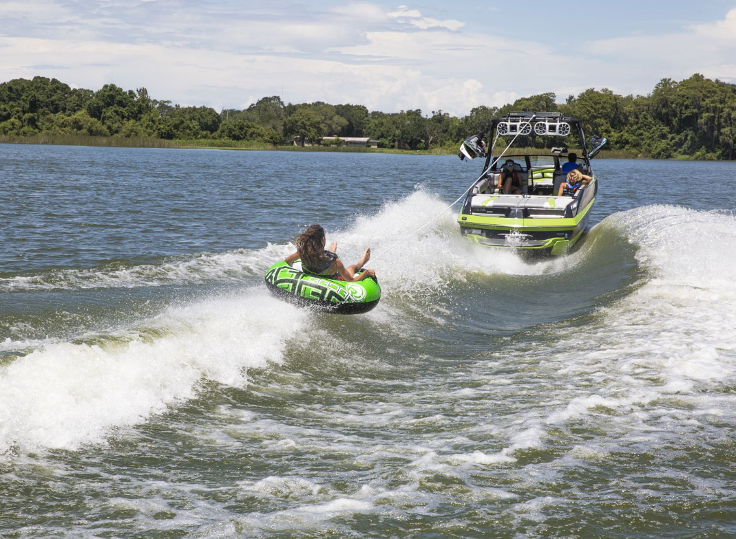 A woman riding a green innertube behind boat's wake.