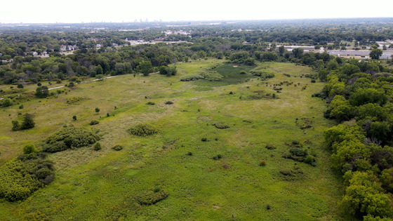 a drone photo of Havenwoods State Forest with lots of grass and vegetation and an urban landscape in the background