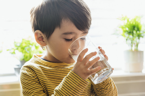 A young boy drinks a glass of water.