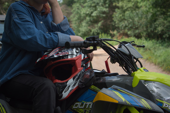 A detailed shot of an ATV rider holding a helmet in their lap while sitting on an ATV. 