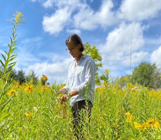 A woman standing in a field of tall grasses and flowers. 