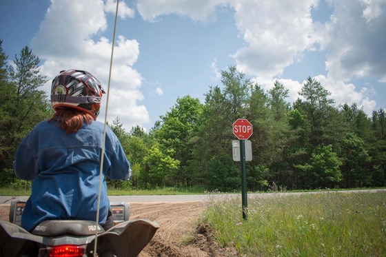 a woman wearing a helmet riding a ATV and stopping at a stop sign