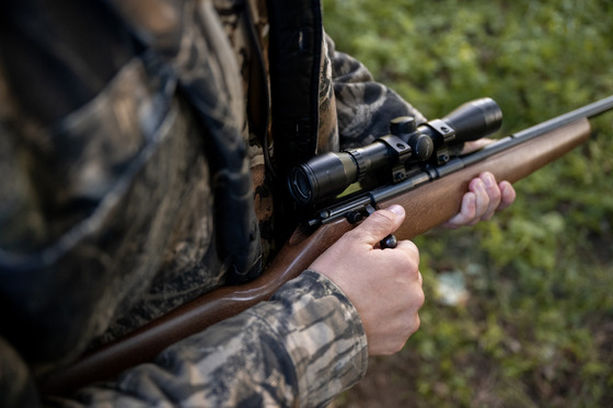 A detail shot of someone holding a rifle in their hands, pointed toward the ground and with their hands outside the trigger guard.