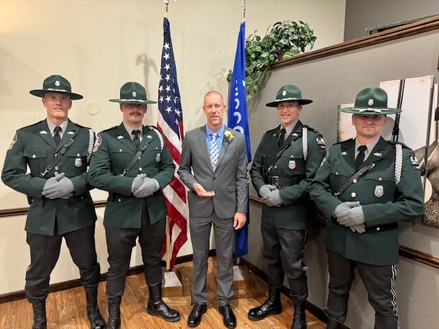 A man in a gray suit poses for a picture with four conservation wardens dressed in formal wear.