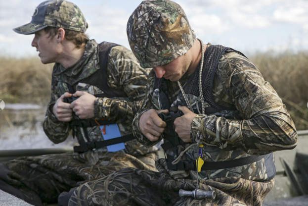 two hunters in camouflage on a boat adjusting their life jackets