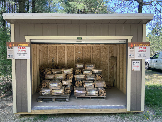 A brown shed with a large open door is filled with bundles of firewood.