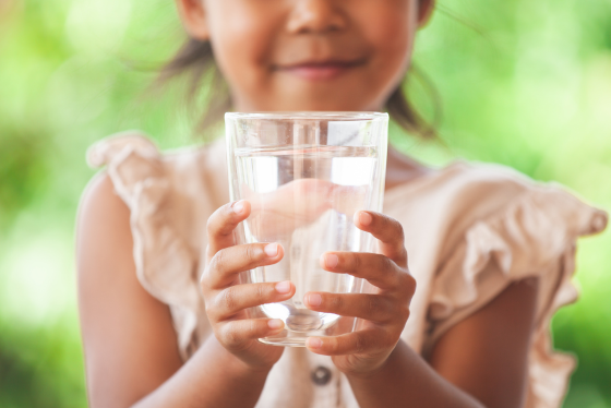 A glass of water is a held in the hands of a girl. 