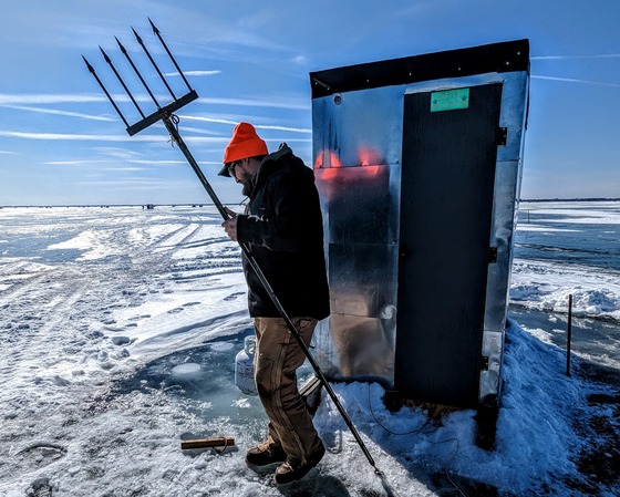 man holding sturgeon spear on frozen lake near ice shanty