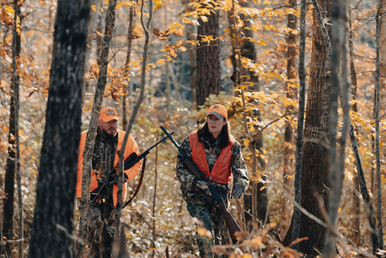 Two hunters wearing blaze orange walk through the woods in autumn. 