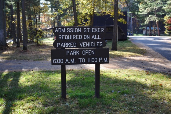 a wooden sign at a Wisconsin state park that says "Admission sticker required on all parked vehicles. Park open 6 a.m. to 11 p.m."