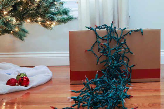 tangled Christmas lights hanging out of a cardboard box near a Christmas tree with ornaments