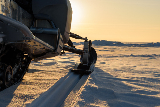 snowmobile on snow at edge of water at sunset