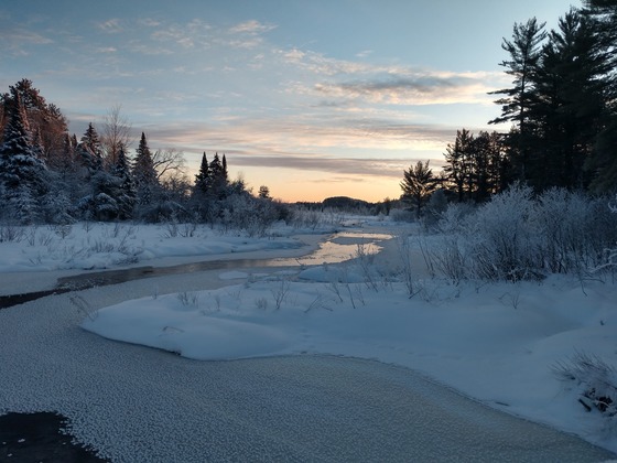 A partially frozen stream winds through a snow-covered landscape.