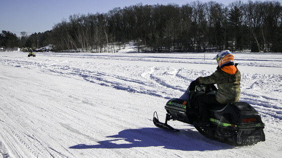 A snowmobiler on a path, going away from the camera.