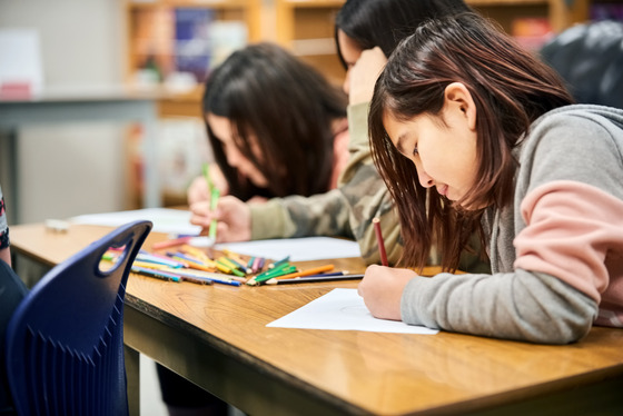 Three students draw at a large desk.