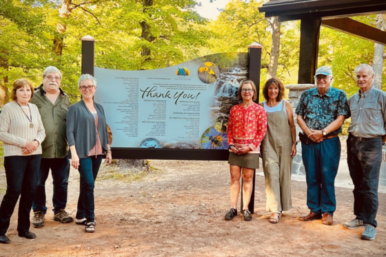 Six people flank a "Thank you" dedication sign at Copper Falls State Park.