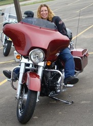 A woman sits on a motorcycle, smiling. 