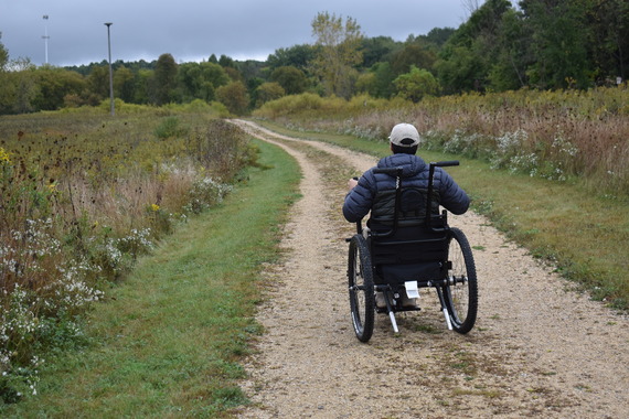 Man in all-terrain wheelchair on a gravel prairie path