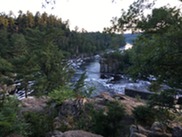 Rocky bluffs covered in evergreen trees tower on either side of a river 