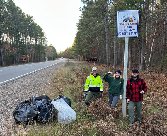 Three people standing next to road with full trash bags