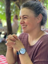 A closeup photo of an individual looking into the distance sitting at a picnic table outside.