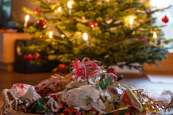 Discarded wrapping paper is shown in front of a holiday tree after gift unwrapping.