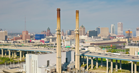 Aerial shot of downtown Milwaukee, Wisconsin on a hazy afternoon in Fall, looking past power plant chimneys and the Marquette Interchange.