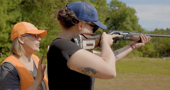 A hunter ed instructor stands by a trainee and instructs her on how to shoot. 