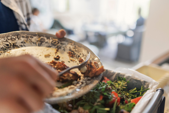 A person scrapes leftover food waste into a compost bin.