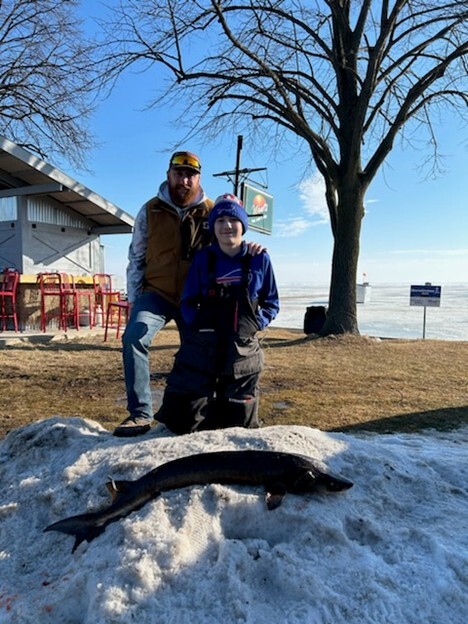 Hoyt Patt standling alongside his dad standing behind a small sturgeon he speared 