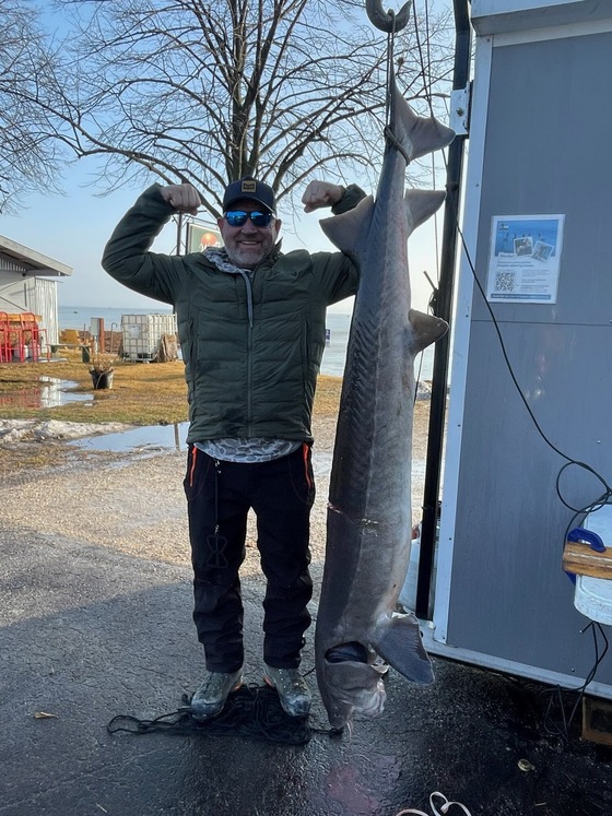 Robert Cave standing next to a speared sturgeon hanging up near a lake