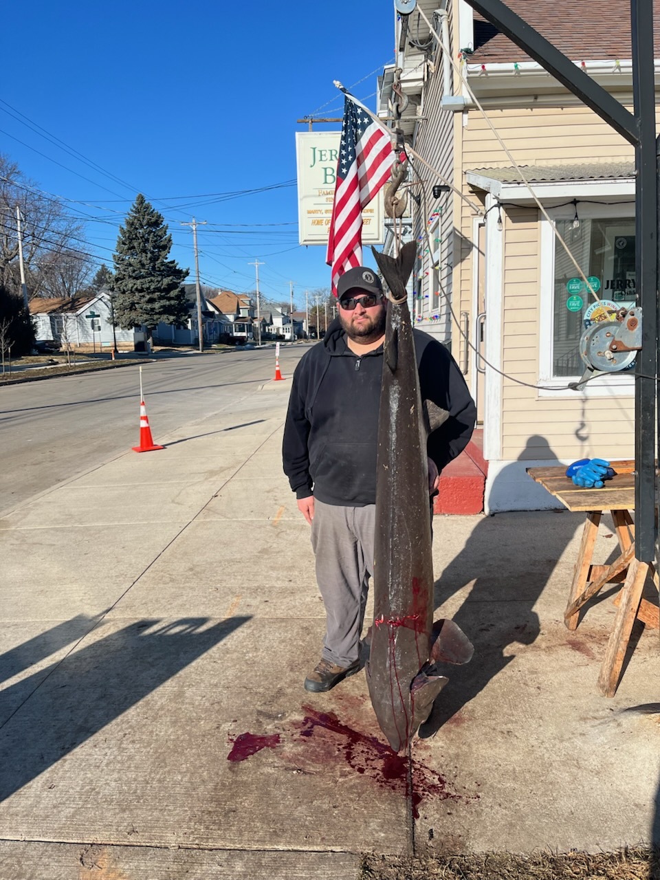 Maxwell Naparalla standing next to speared sturgeon being weighed in downtown Oshkosh