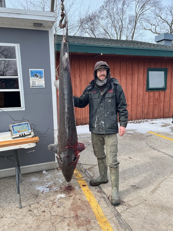 Trevor Theyerl standing next to a hanging sturgeon that has been speared