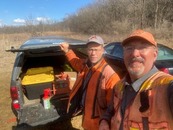 Two men smile at the camera in front of an open car trunk. 