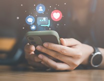 Graphic depicting a person's hands holding a cell phone with various emojis surrounding the phone