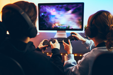 Two friends wearing headsets gaming on computer