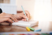 Hand writing in notebook with blue pencil on a desk
