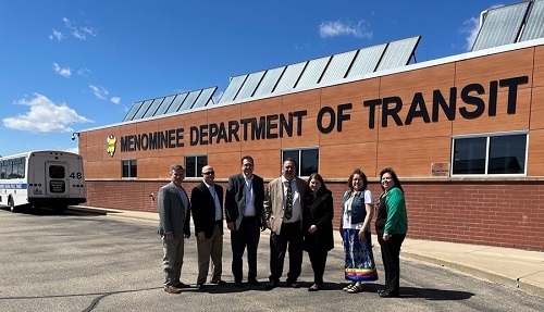 DOA and Menominee Tribal representatives outside Menominee Department of Transit Services building, with solar panels on top. 
