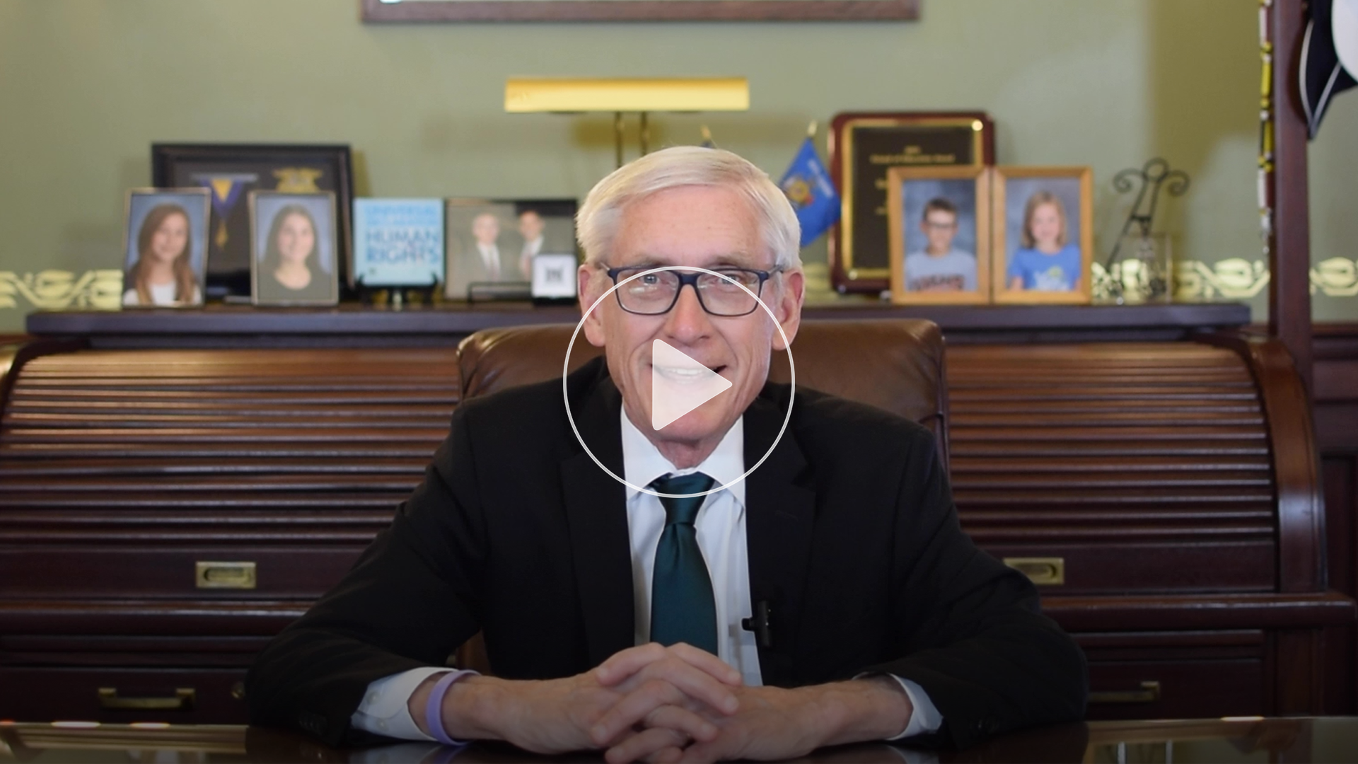 Photo of Gov. Evers at his desk with a video play button.