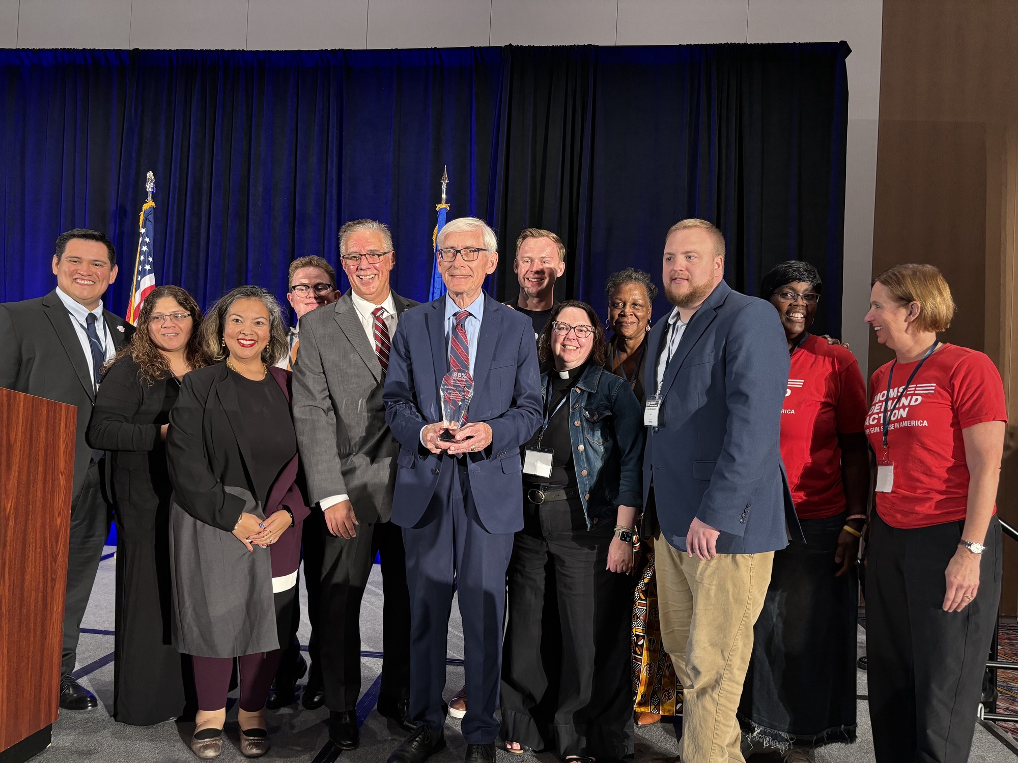 Gov. Evers poses for a photo with stakeholders of the 80% Coalition with award