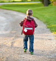 Boy walking with backpack on dirt road 