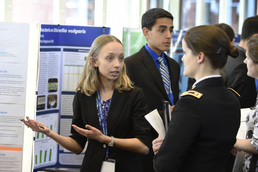 Female student explaining science project to a female Army officer