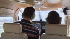 Pilot and student pilot in cockpit of plane flying over landscape