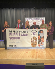 People hold a banner to celebrate the Wyoming Purple Star School designation.