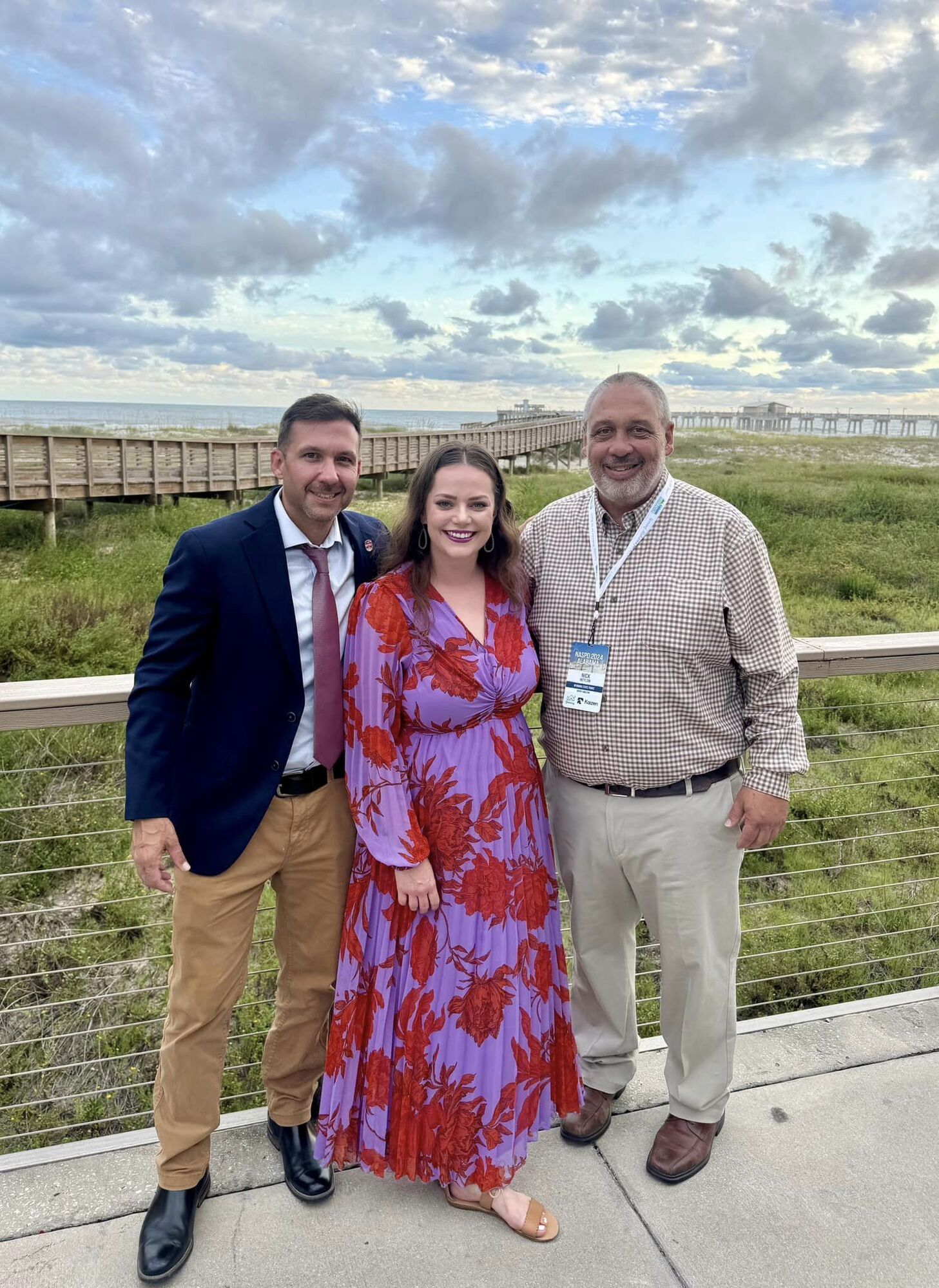 Two men and one woman dressed up with beach in the background at sunset.